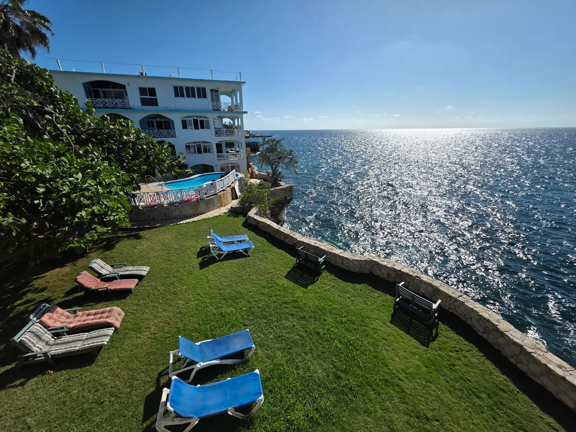 The lawn, loungers and cliffside pool above the sea at Home Sweet Home Resort