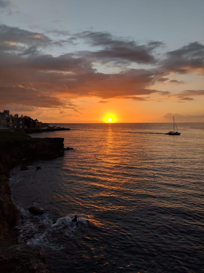 A sailboat crossing the sunset off the West End cliffs